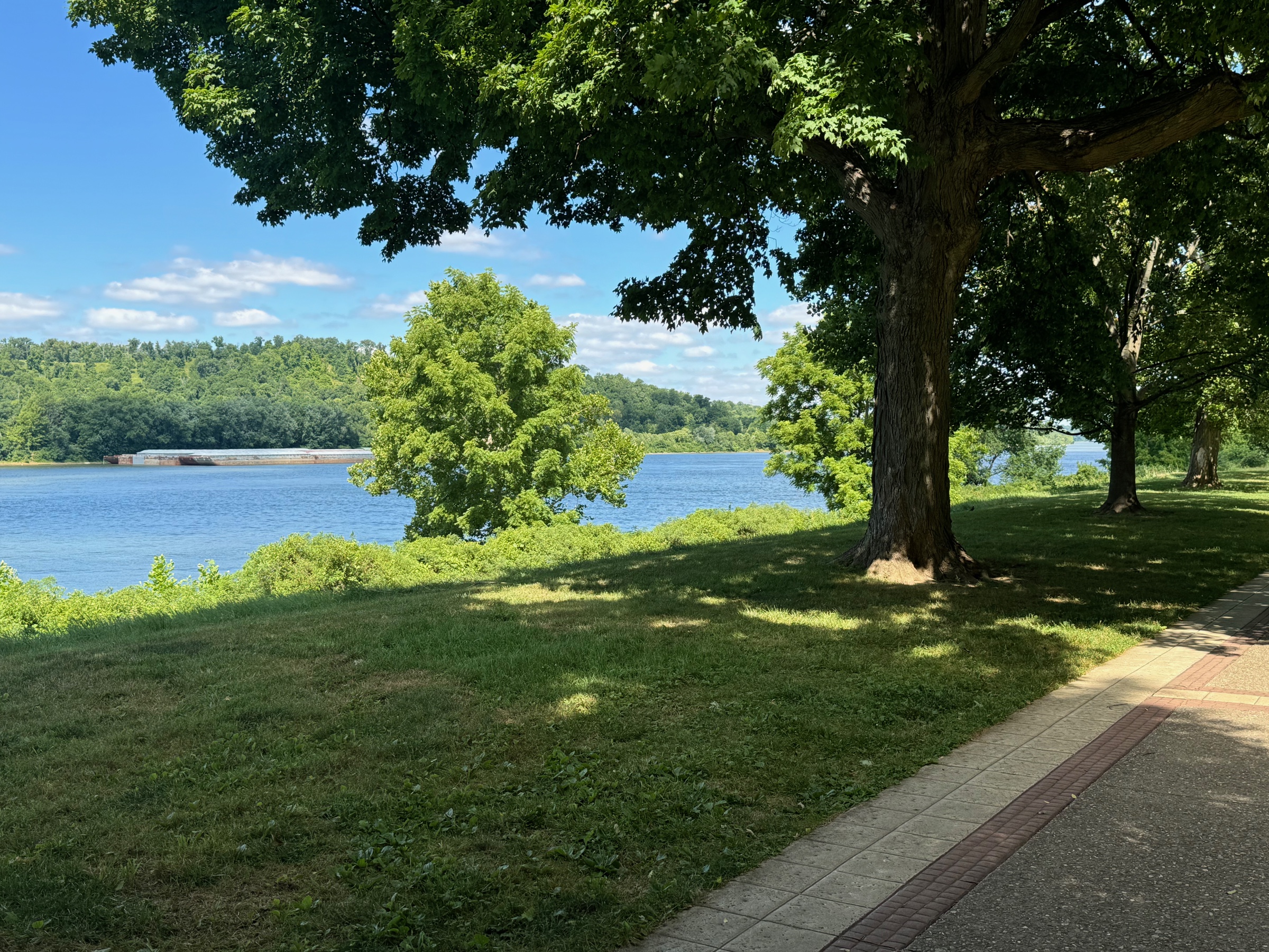 Ohio River park in Cincinnati — walkway, barge, and wooded far bank